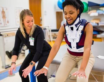 two woman practice movements while one wears a back brace
